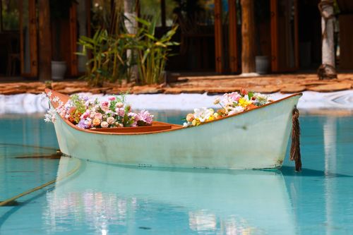 Free A serene scene of a canoe filled with vibrant flowers floating on a clear blue pool. Stock Photo