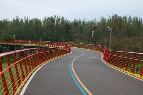 Free A vibrant pathway with red railings winding through a green landscape, ideal for outdoor activities. Stock Photo