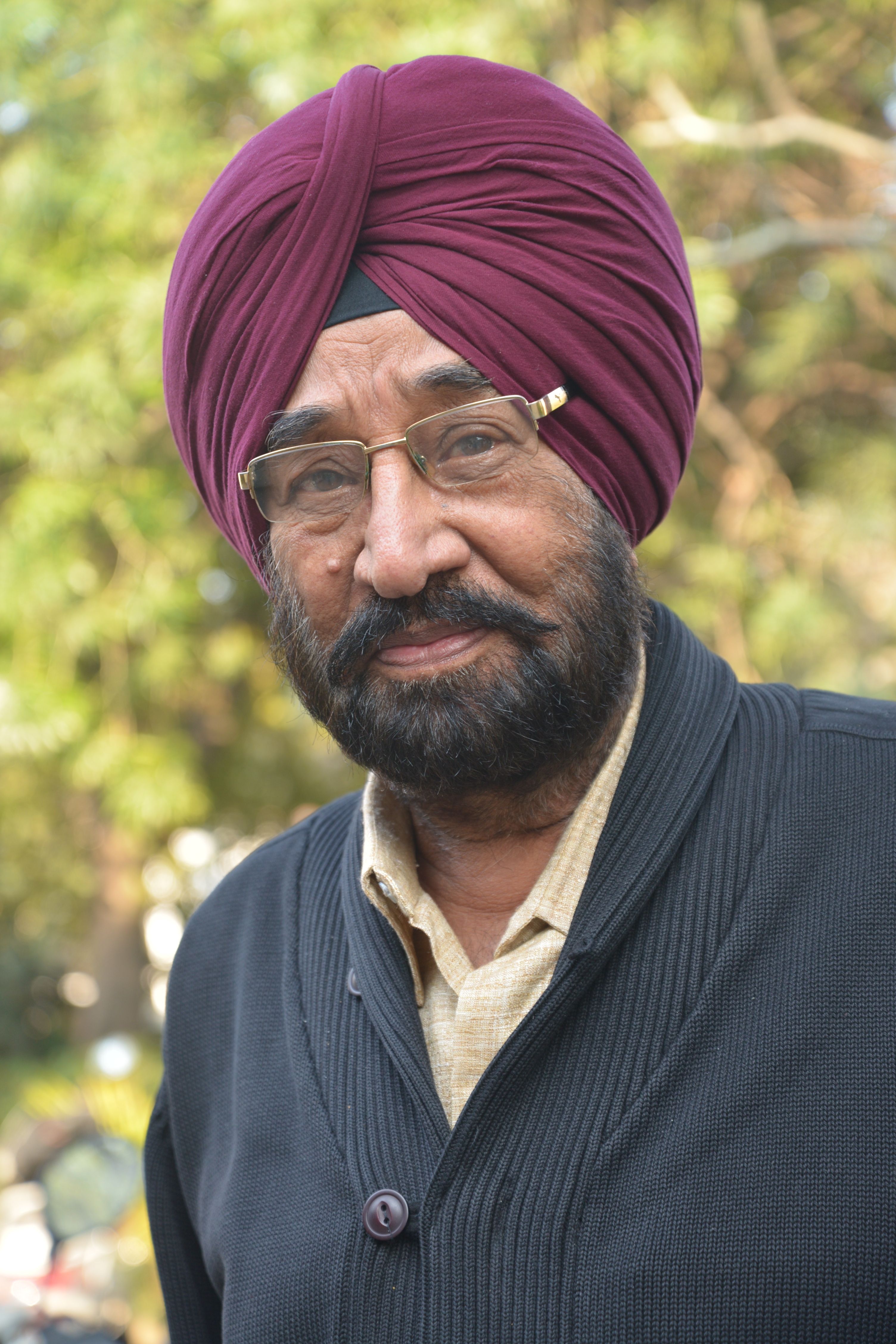 Close-up portrait of a senior man wearing a turban in a park setting, displaying a warm smile.