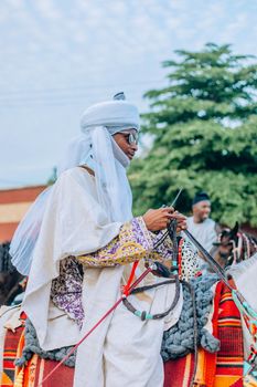 Man in traditional African attire riding a horse during a colorful cultural festival.