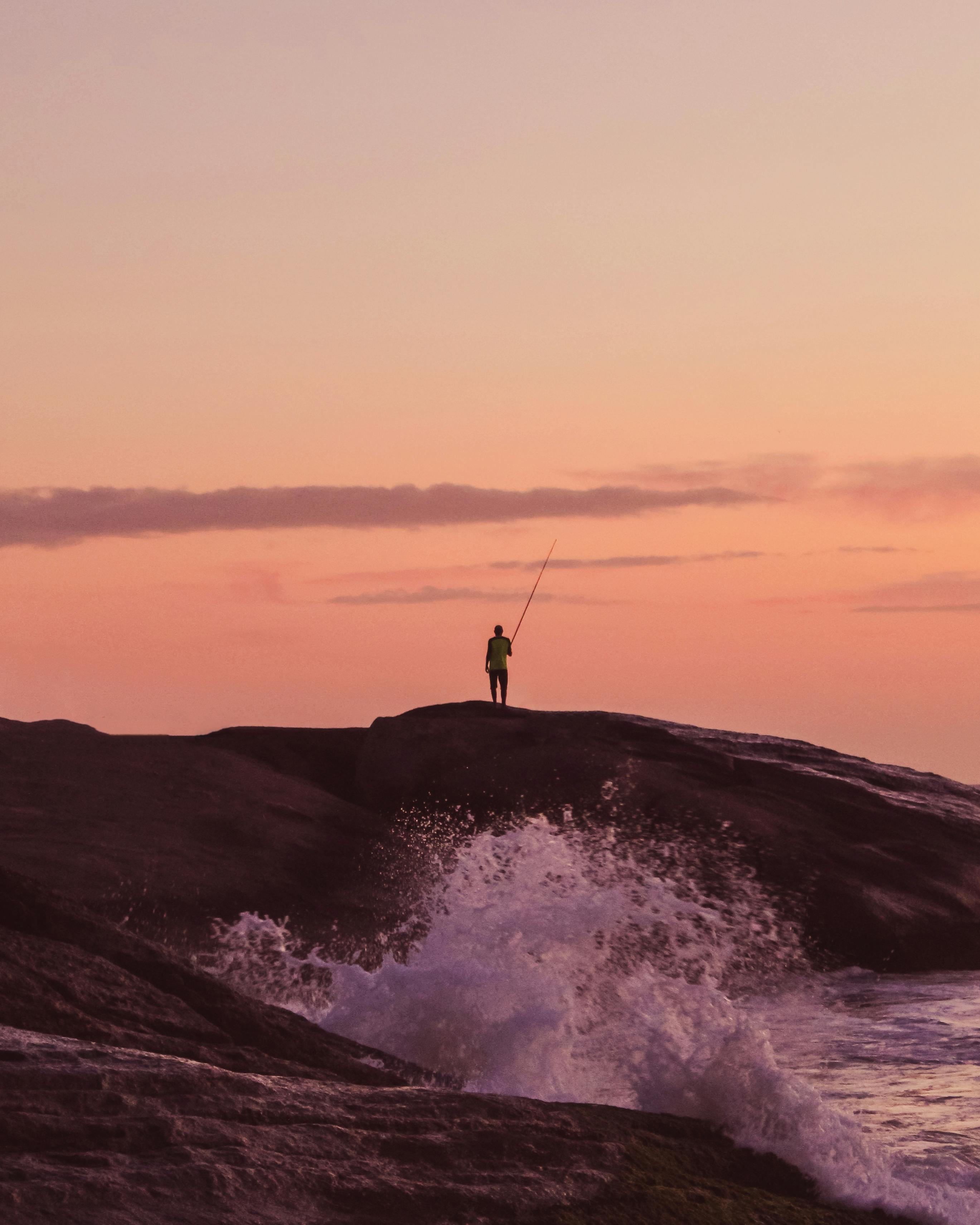 在岩石悬崖上，一名渔夫的轮廓映衬着充满活力的日出