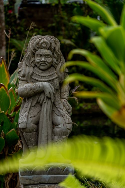 Free Artistic stone statue surrounded by lush green foliage in a serene garden setting. Stock Photo