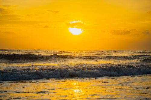 Free Dramatic sunset casting golden hues over ocean waves, captivating a tranquil beach view. Stock Photo