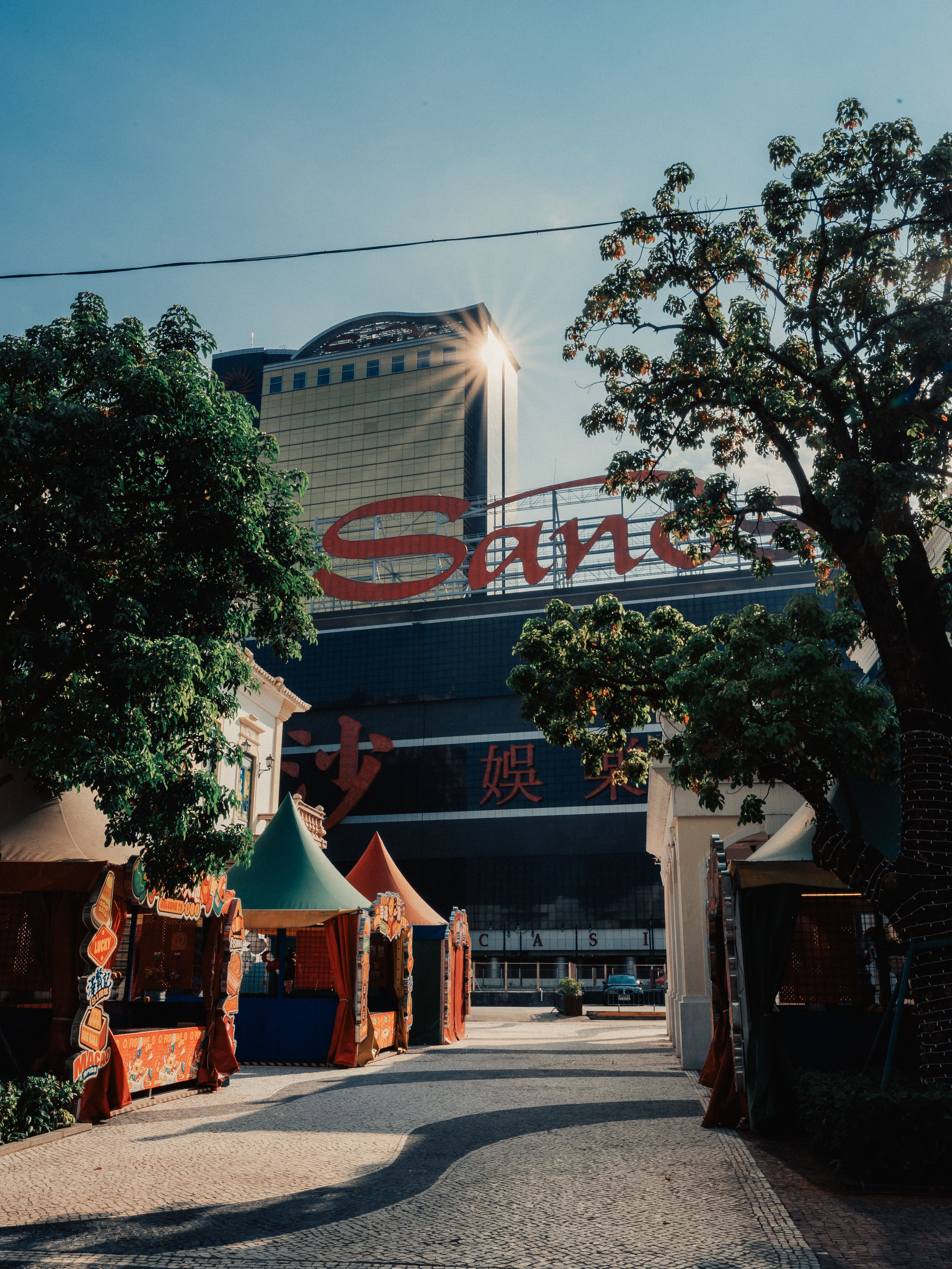 Street view of Sands Resort in Macao with morning sunlight, trees, and vibrant tents.