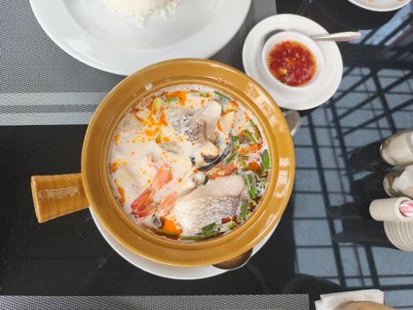 A flavorful bowl of Thai Tom Yum soup with seafood served alongside rice and chili sauce.