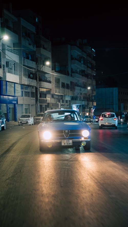 Free Vintage car driving through a quiet city street at night, capturing a nostalgic urban mood. Stock Photo