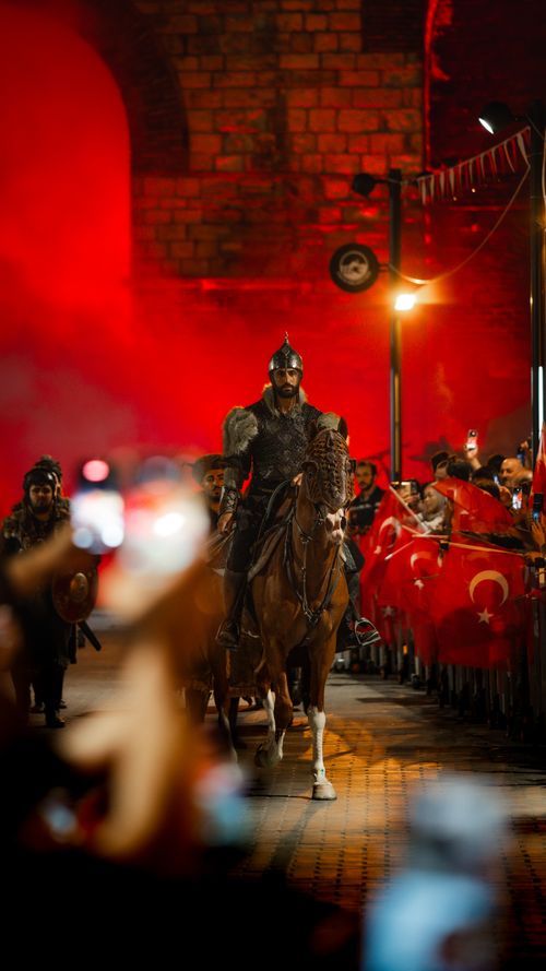 Free Knight on horseback during a historical parade surrounded by Turkish flags, vibrant evening atmosphere. Stock Photo