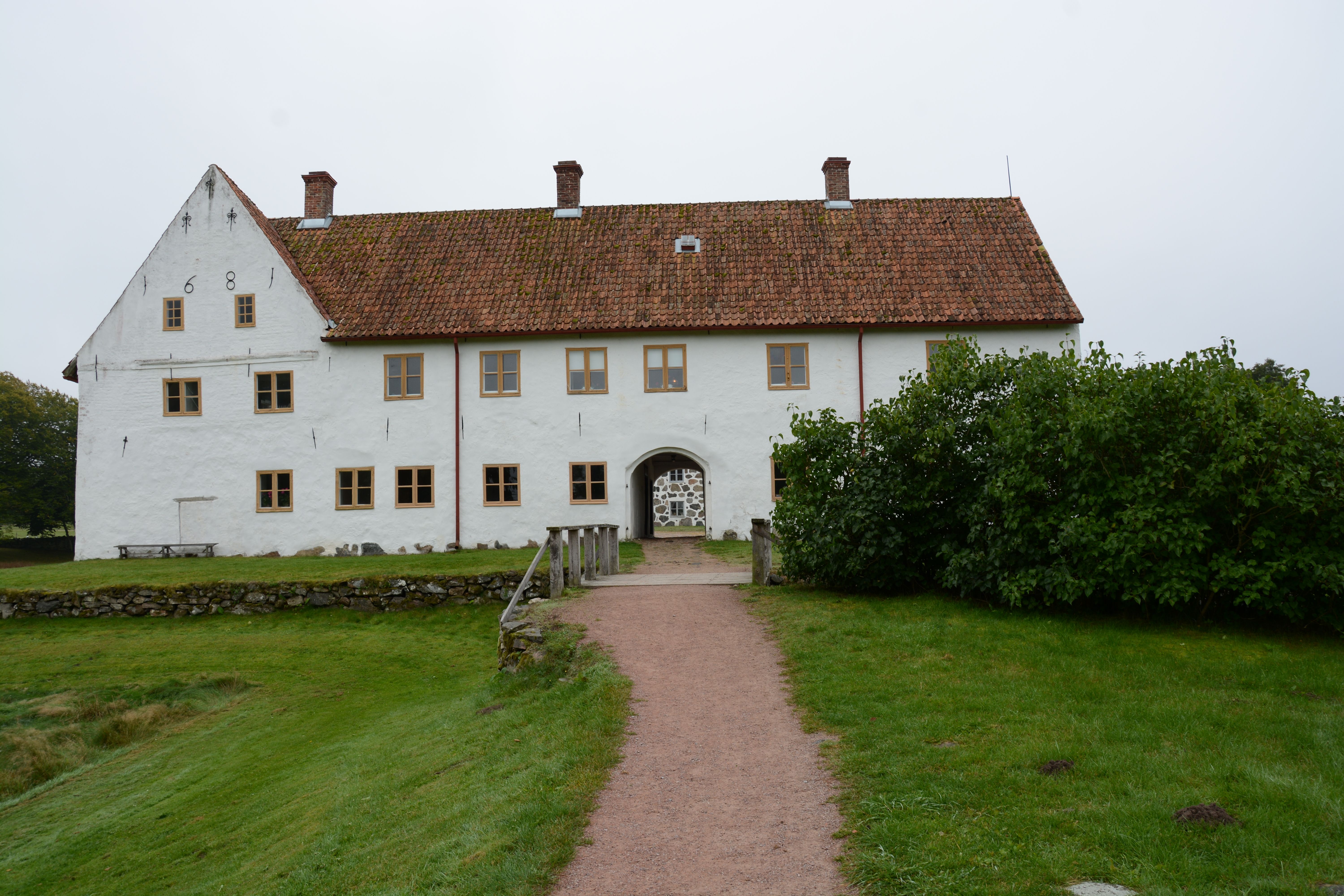 Charming white manor house with rustic roof in verdant countryside setting.