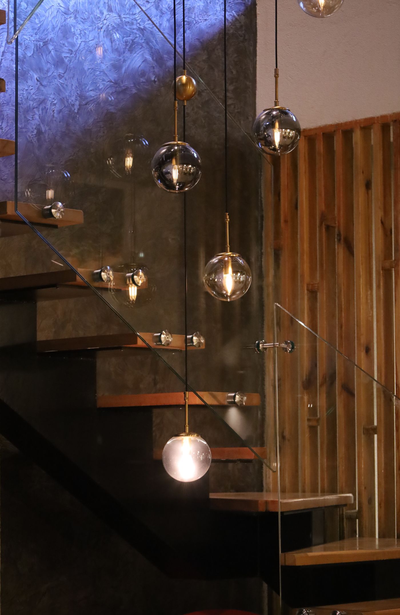 Timber stair lit by glass pendant lights against a dark stone wall
