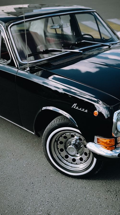 Free A close-up of a classic vintage car showcasing its shiny black finish and chrome details, parked outdoors. Stock Photo