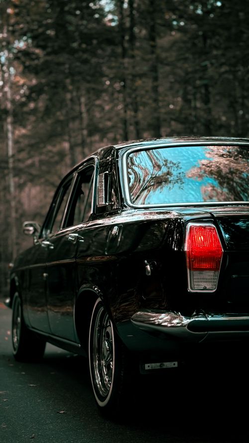 Free A vintage car parked on a forest road, reflecting trees in autumn. Stock Photo