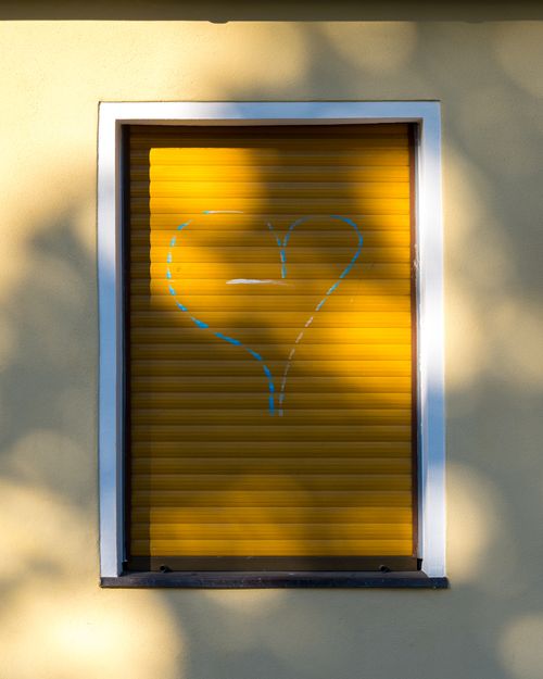 Free A heart graffiti on a closed yellow window shutter casts shadows on the wall. Stock Photo