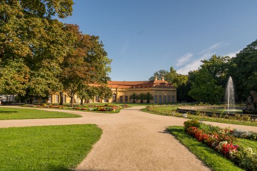 Free Beautiful European garden scene with historic building, fountain, vibrant flower beds, and lush greenery under clear skies. Stock Photo