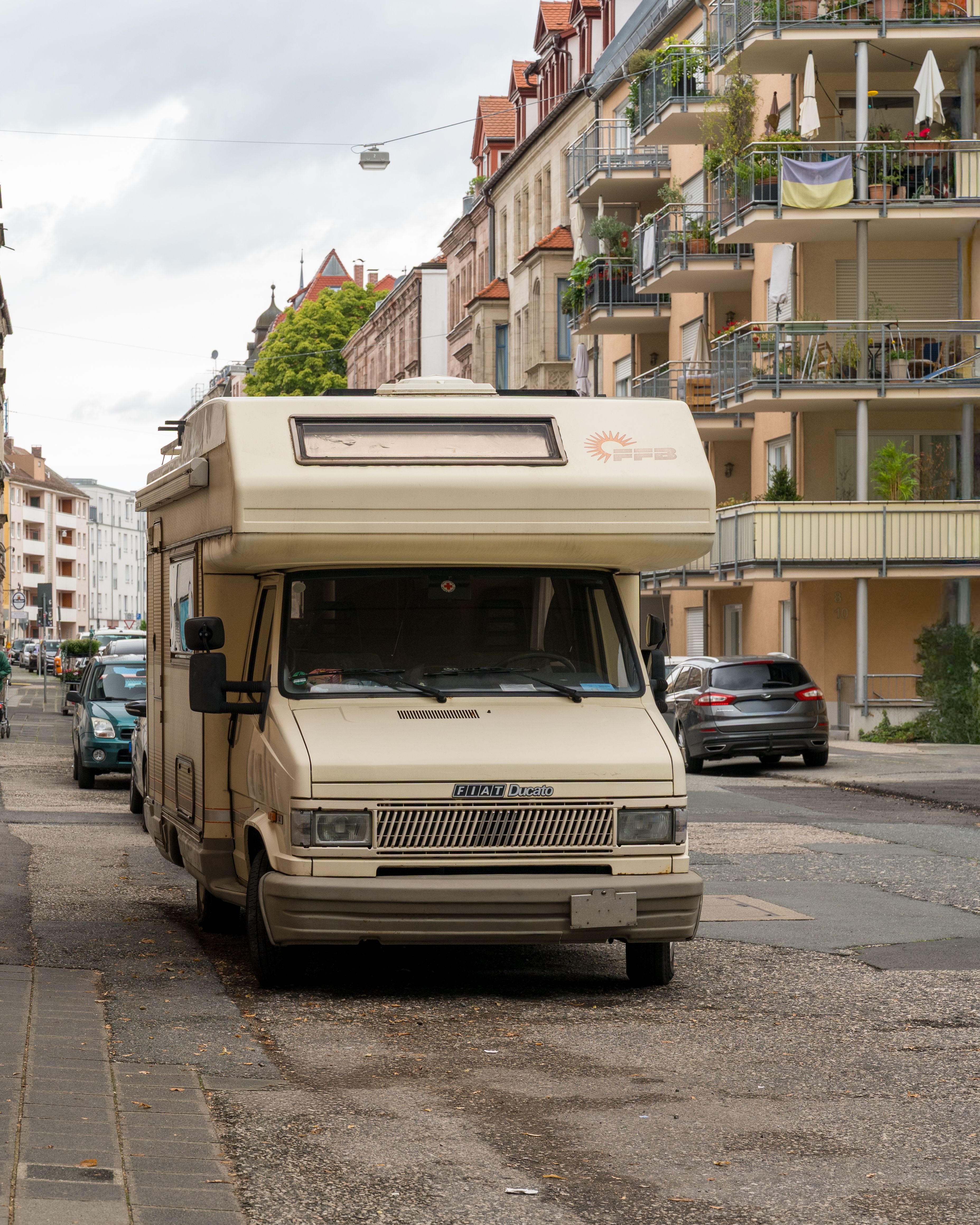 A classic Fiat camper van parked on a charming European city street with historic architecture.