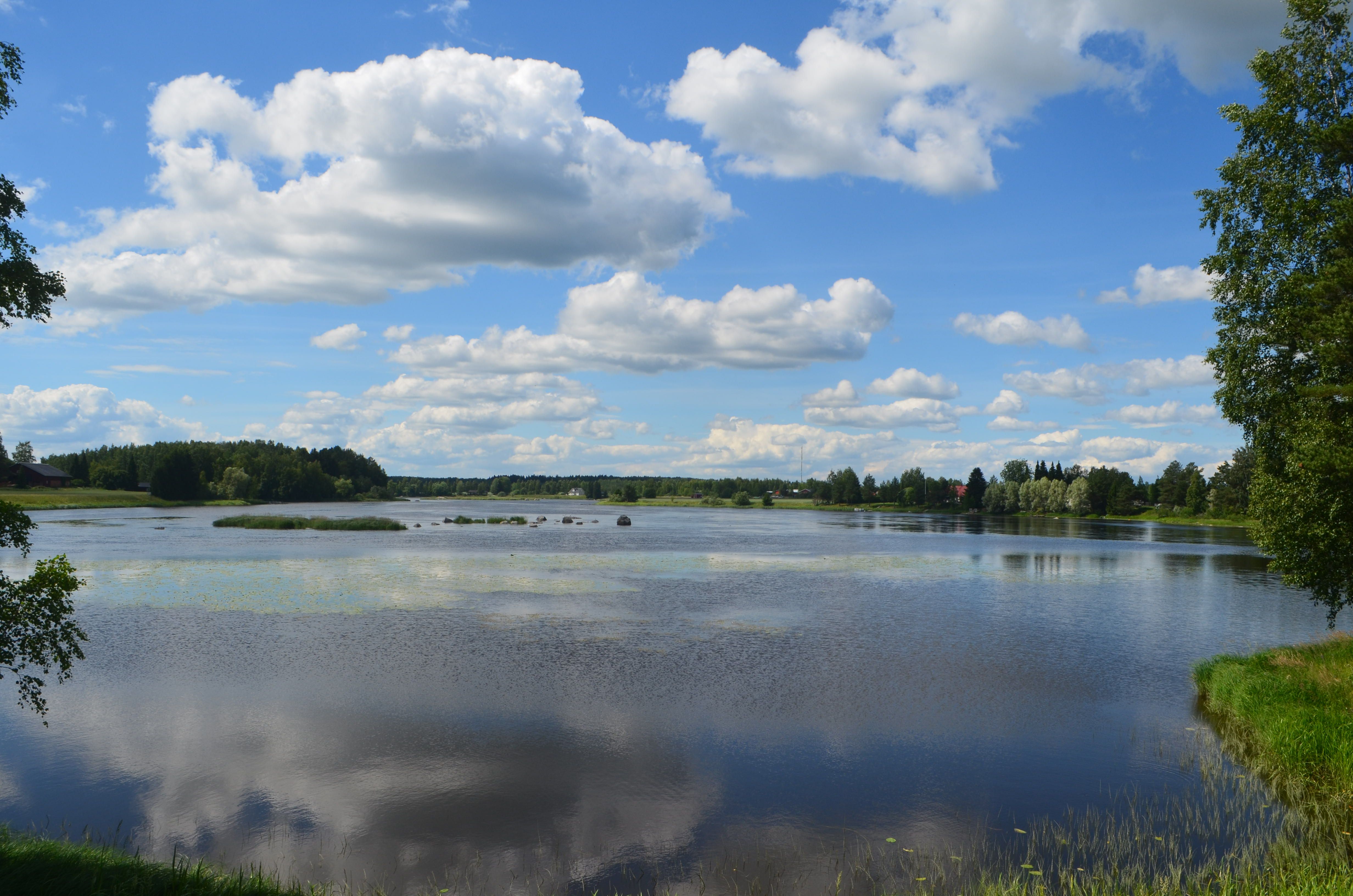 Peaceful lake scene in Finland with reflection of clouds and lush greenery.