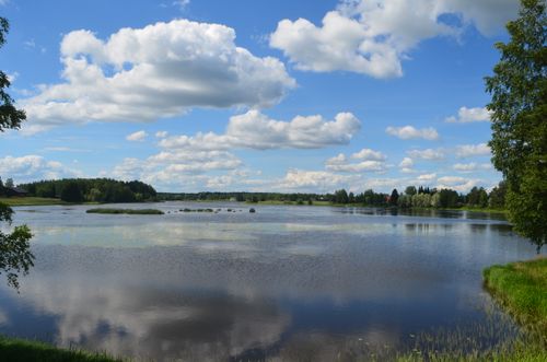 Free Peaceful lake scene in Finland with reflection of clouds and lush greenery. Stock Photo