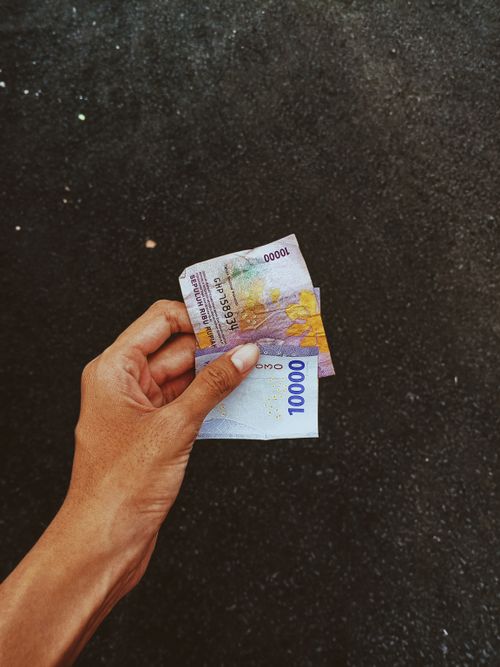 Free A close-up of a hand holding currency notes against a dark surface, emphasizing finance and economy. Stock Photo