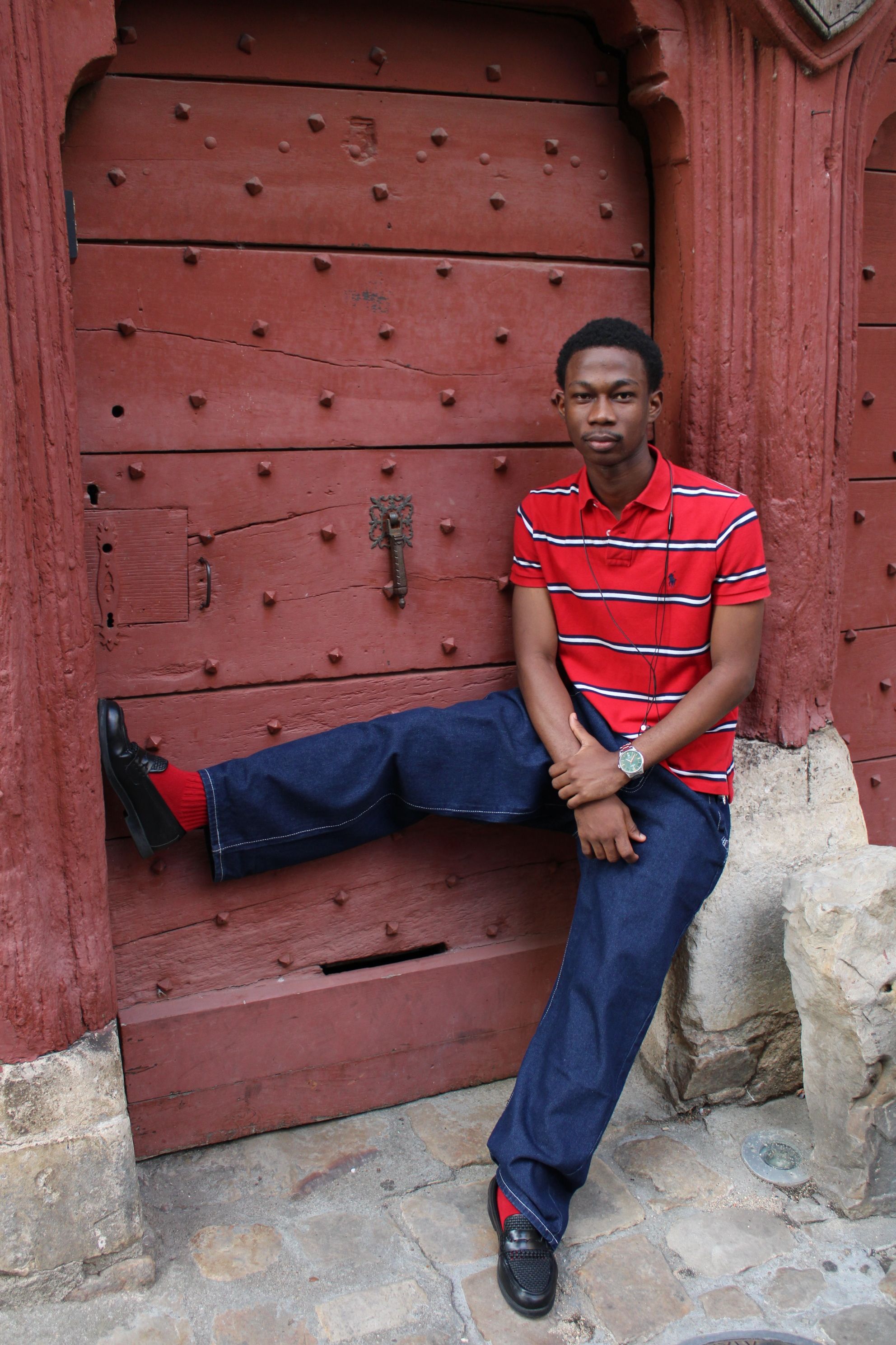 Stylish young man in red shirt and jeans leaning on a historic wooden door.