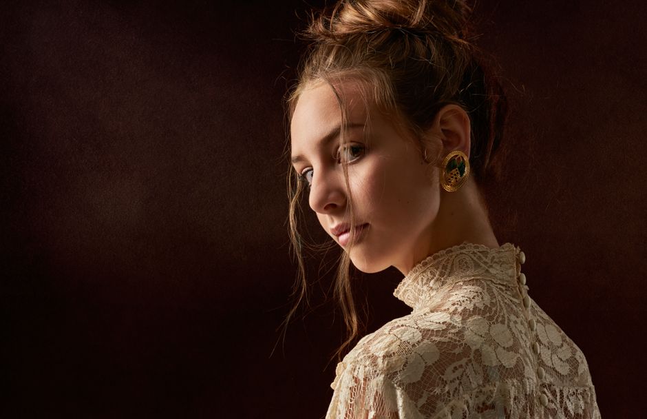 Portrait of a young woman with elegant hairstyle and lace dress, showcasing vintage earrings.