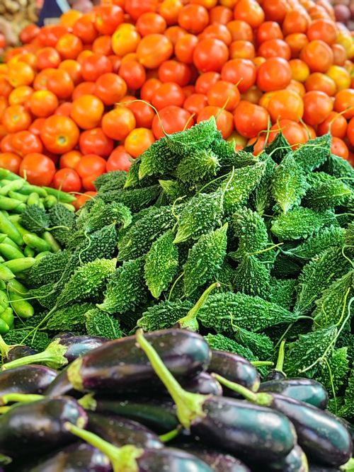 Free Colorful assortment of tomatoes, bitter melons, and eggplants at a market. Stock Photo