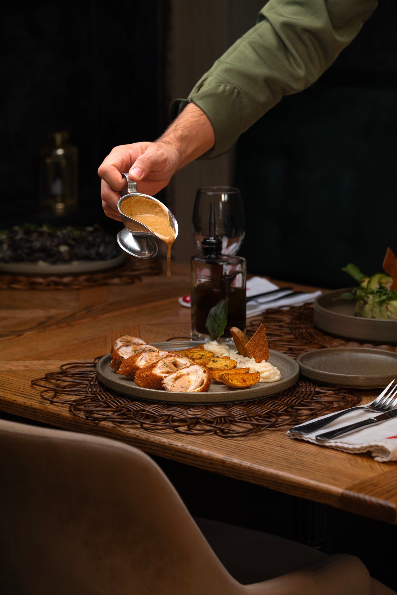Hand pouring gravy from a small gravy boat over a plated dinner