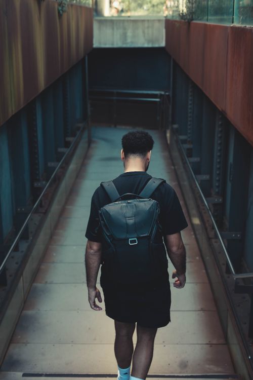 Free Man with a backpack walking down a modern urban tunnel, illustrating a sense of exploration. Stock Photo