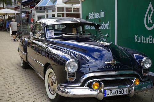 Free Classic navy blue Oldsmobile car parked on a modern street setting. Stock Photo