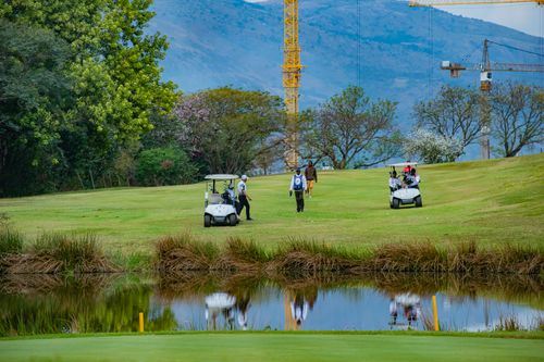 Free Golfers enjoying a serene game on a lush course in Piggs Peak, Eswatini, with scenic mountain views. Stock Photo