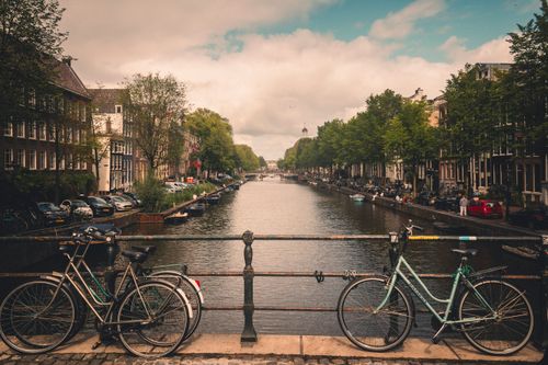 Free Peaceful view of Amsterdam's iconic canals with bicycles on a bridge under a cloudy sky. Stock Photo