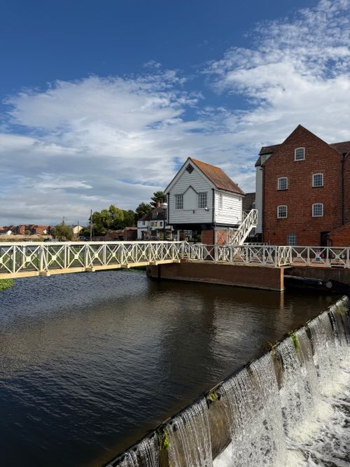 Free Charming riverside scene with historic mill, bridge, and clear blue sky. Stock Photo