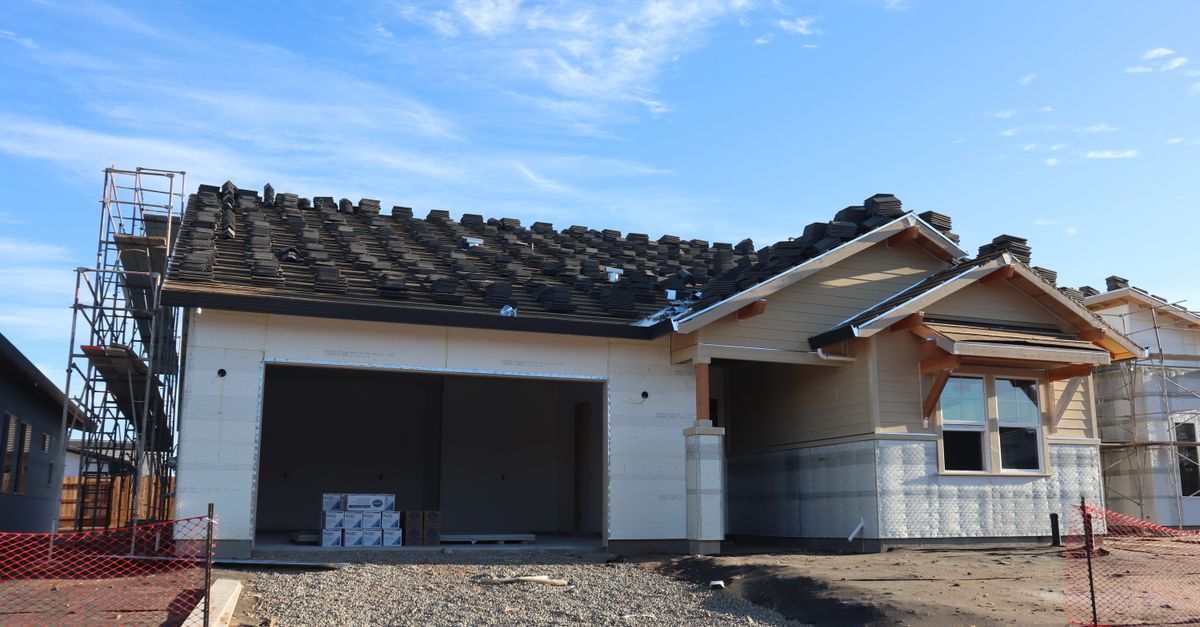 Modern house under construction with visible scaffolding and tiles on roof.