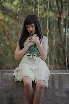 一名年轻女子身穿白色连衣裙，抱着娃娃在宁静的森林中沉思
