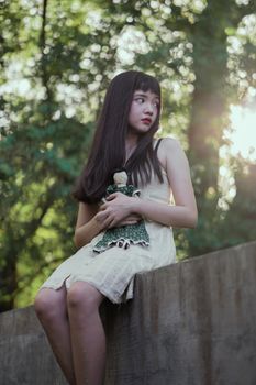 一名年轻女子手拿娃娃坐在户外，自然光透过树木洒落在她身上