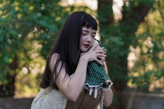 一位长发年轻女子在户外抱着一个娃娃，四周绿植环绕