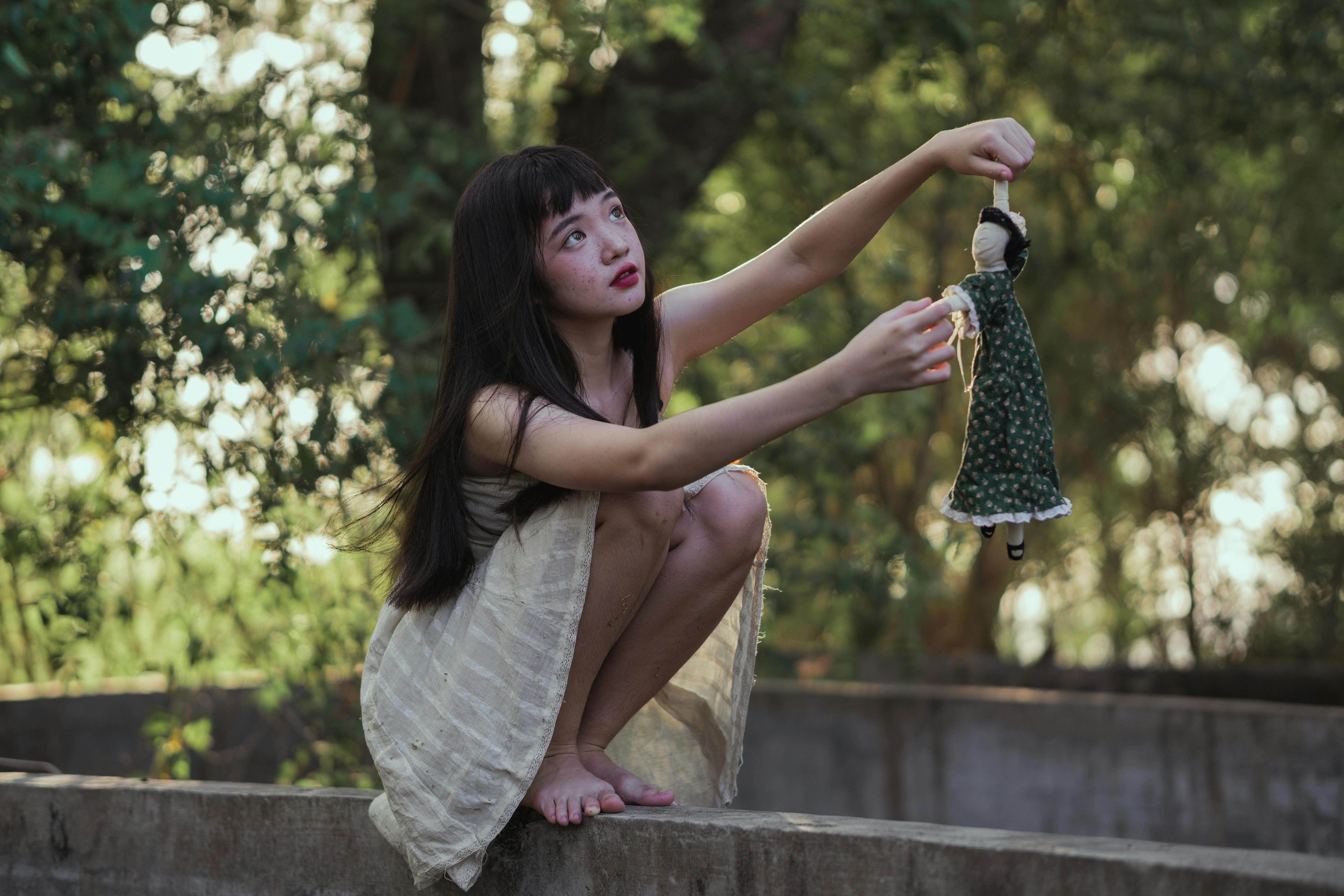 一名年轻女子蹲在宁静的户外，玩着一个古董娃娃