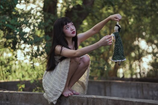 一名年轻女子蹲在宁静的户外，玩着一个古董娃娃