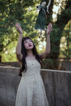 一名身穿白色连衣裙的女子在树木繁茂的户外扔了一个娃娃