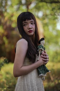 一个长发年轻女孩抱着复古娃娃，在宁静的户外环境中流露出沉思的心情