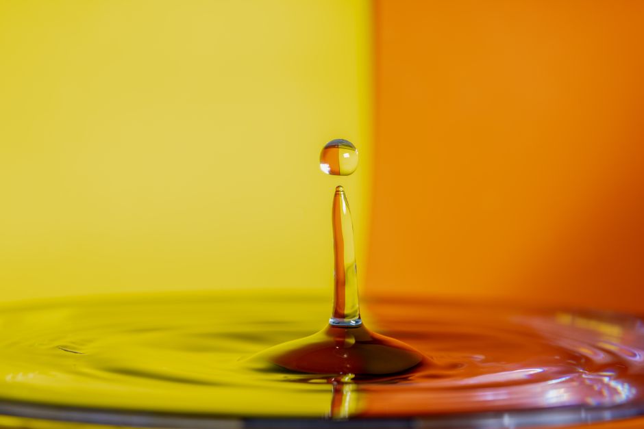 Dynamic capture of a water droplet with vibrant yellow and orange hues in the background.