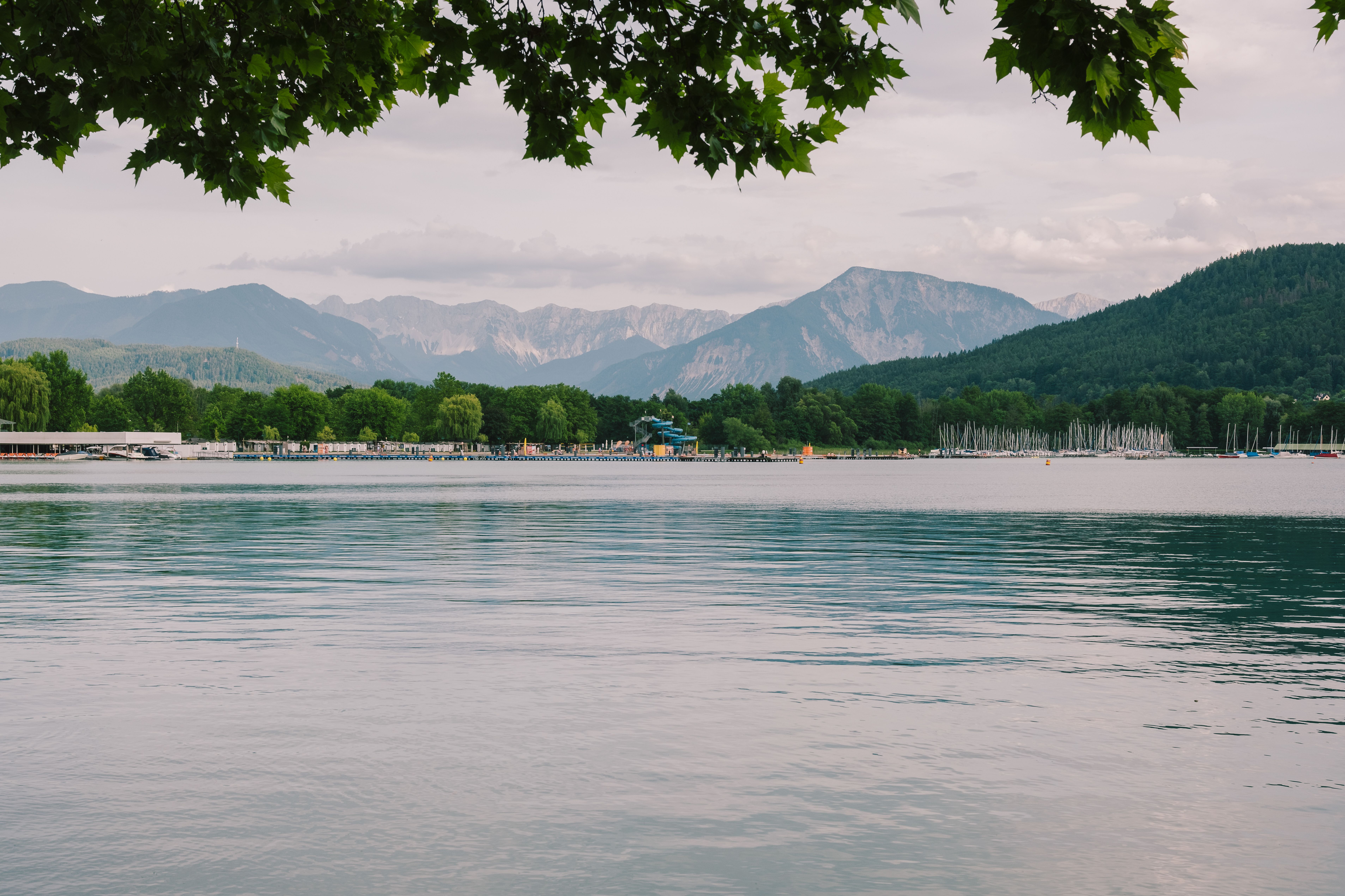 Serene view of Lake Wörthersee with distant mountains and lush greenery in Klagenfurt, Austria.