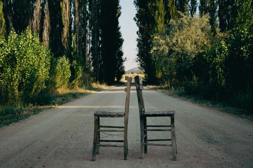 Free Two wooden chairs facing each other on a serene, tree-lined dirt road. Stock Photo