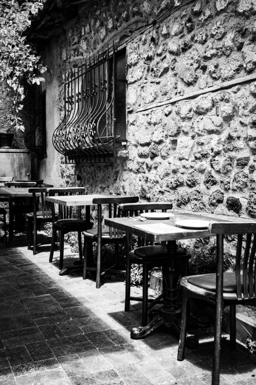 Free Rustic outdoor European cafe with stone wall, vintage chairs, and tables in black and white. Stock Photo