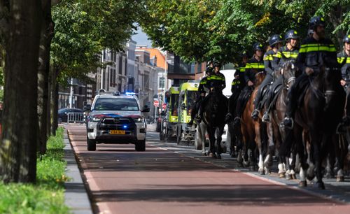 Free Police vehicle and officers on horseback patrol a tree-lined urban street, ensuring public safety. Stock Photo