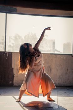 在室内，一位女士优雅地表演着当代舞蹈，自然光线凸显了她的身姿