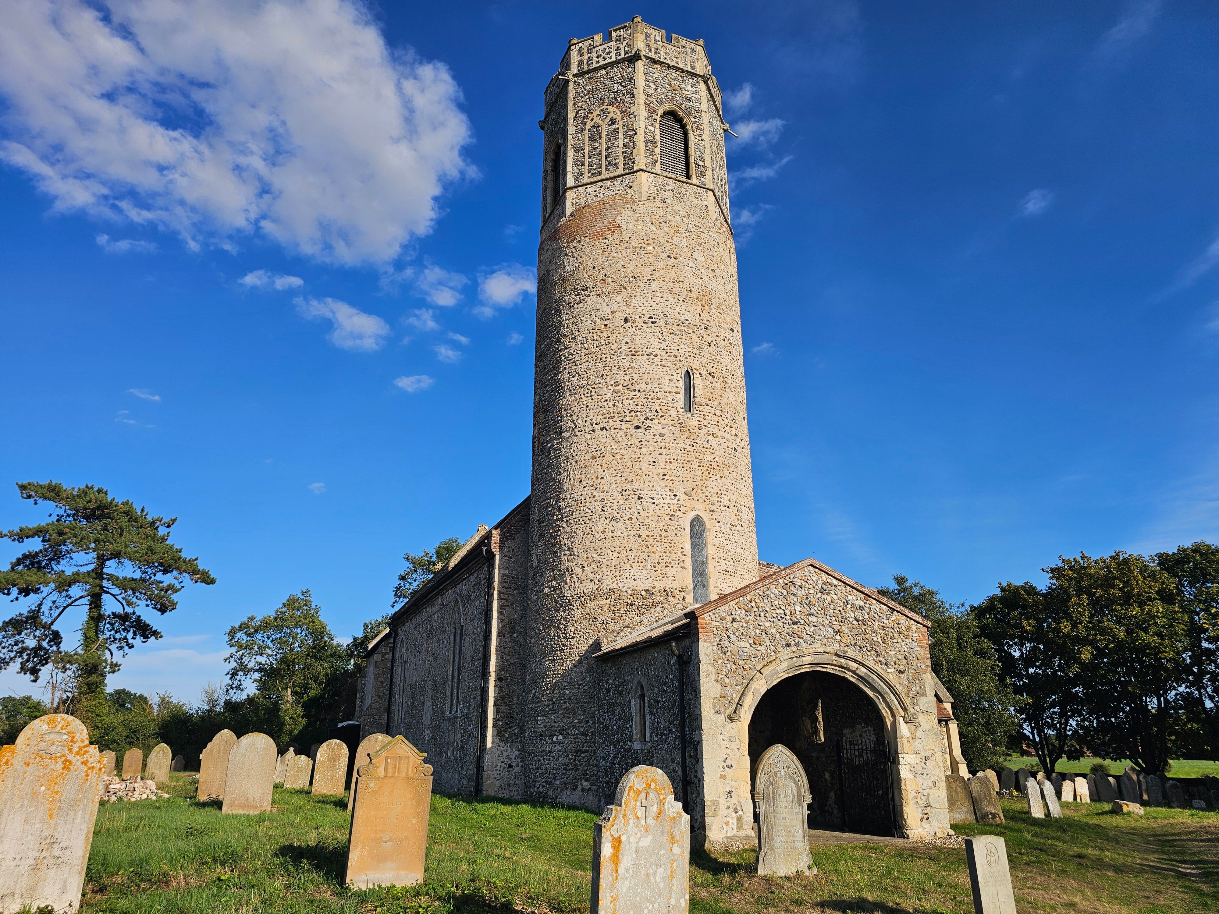 Image of the historic round tower church in Mutford, England under a bright blue sky.