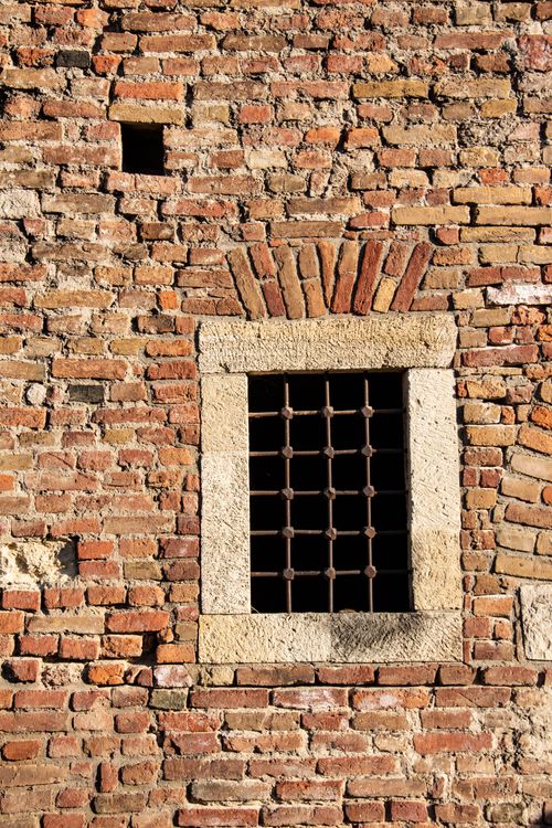 Free Detailed view of a historic brick wall featuring a small, iron-grated window in sunlight. Stock Photo