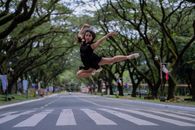 芭蕾舞演员在一条绿树成荫的风景优美的道路上空跳跃