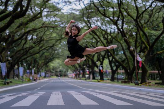芭蕾舞演员在一条绿树成荫的风景优美的道路上空跳跃