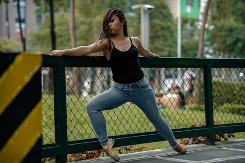 Woman In Black Tank Top And Blue Denim Jeans Holding On A Fence