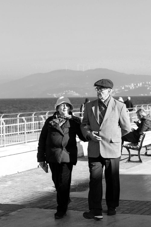 Free A senior couple strolls on a seaside promenade on a sunny day, showcasing companionship and leisure. Stock Photo